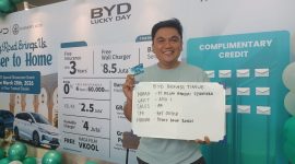 Seorang konsumen berpose sambil menunjukkan kartu dan papan informasi setelah mengikuti program promo BYD Lucky Day di Bekasi Timur, Sabtu (28/3/2026). Program ini menawarkan berbagai keuntungan seperti asuransi gratis hingga 3 tahun, wall charger gratis, serta hadiah langsung berupa power bank Baseus bagi pelanggan yang melakukan pembelian unit.