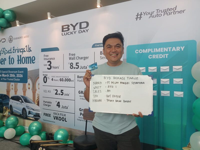 Seorang konsumen berpose sambil menunjukkan kartu dan papan informasi setelah mengikuti program promo BYD Lucky Day di Bekasi Timur, Sabtu (28/3/2026). Program ini menawarkan berbagai keuntungan seperti asuransi gratis hingga 3 tahun, wall charger gratis, serta hadiah langsung berupa power bank Baseus bagi pelanggan yang melakukan pembelian unit.