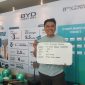Seorang konsumen berpose sambil menunjukkan kartu dan papan informasi setelah mengikuti program promo BYD Lucky Day di Bekasi Timur, Sabtu (28/3/2026). Program ini menawarkan berbagai keuntungan seperti asuransi gratis hingga 3 tahun, wall charger gratis, serta hadiah langsung berupa power bank Baseus bagi pelanggan yang melakukan pembelian unit.