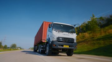 Isuzu GIGA mengangkut kontainer melaju di jalan tol, menjadi salah satu kendaraan komersial yang mendukung aktivitas logistik dan distribusi barang di Indonesia.