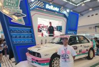 Brand Strategi Belkote, Gimy Bayu, berpose di depan mobil reli milik Rifat Sungkar yang menggunakan cat Belkote di booth IMX 2026, Jumat (9/10/2026).