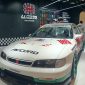 Sebuah Honda Accord bergaya racing dengan balutan warna putih, merah, dan hijau yang tampil mencolok di sebuah pameran otomotif. Mobil ini dilengkapi dengan body kit sporty, velg racing berwarna hijau, serta berbagai stiker khas motorsport. Latar belakangnya menampilkan booth modifikasi mobil dengan dekorasi bernuansa hitam dan logo Spider. Perpaduan desain klasik dan sentuhan modifikasi modern membuat mobil ini terlihat unik, agresif, dan penuh karakter.